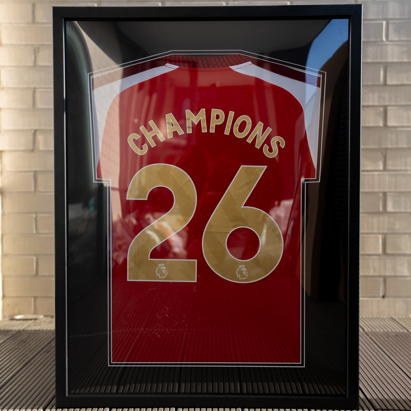 Black framed red football shirt personalised with CHAMPIONS and the number 26 in gold lettering