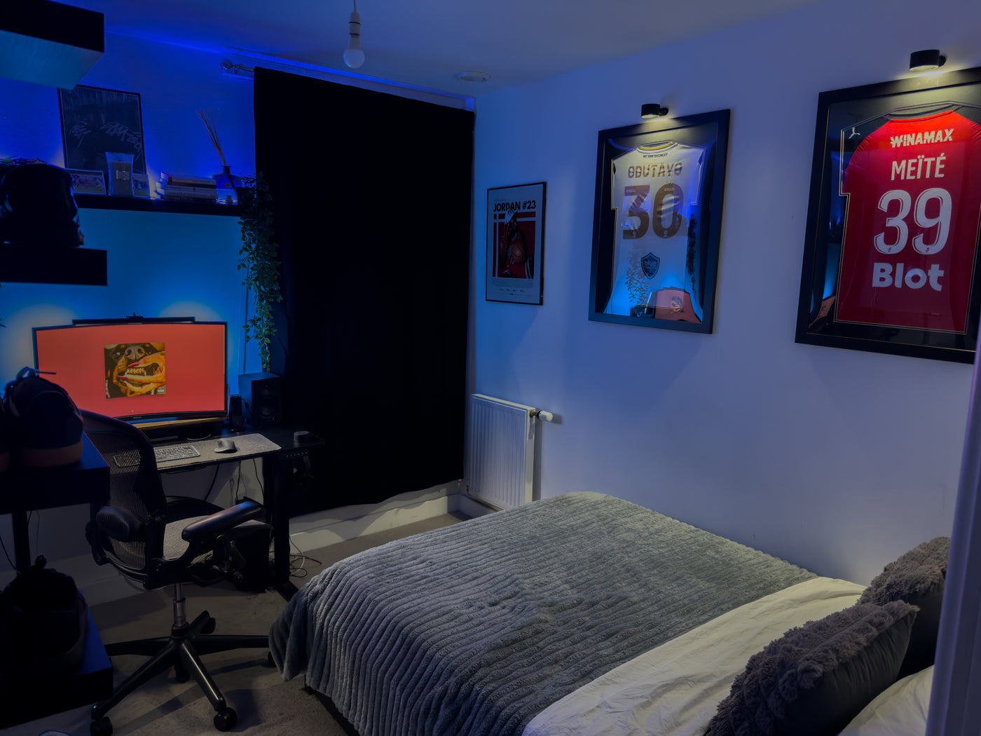 Two black framed football shirts hanging above a bed in a bedroom, each personalised with a name and number